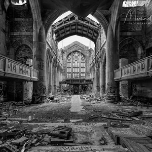 May include: Black and white photograph of an abandoned church interior. The image shows the decaying structure with broken wooden beams, graffiti, and crumbling walls. The arched ceiling and large windows are still visible.