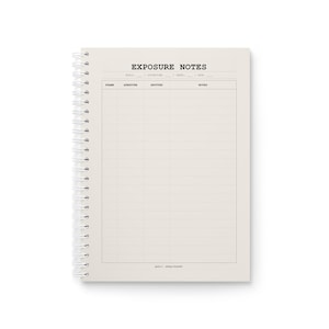 Op de afbeelding: Een spiraalgebonden notitieboek met een crèmekleurige kaft met de tekst EXPOSURE NOTES bovenaan. De pagina bevat gedrukte velden voor rol, locatie, datum en ASA, gevolgd door een tabel met kolommen voor frame, diafragma, sluitertijd en notities.