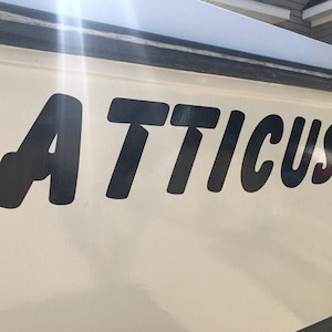 May include: A white boat with the name "ATTICUS" written in large, black, bold letters on the side.