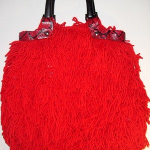 Może przedstawiać: Czerwona torebka z czarnym uchwytem i wzorem skóry węża na górnej klapie.