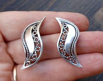 May include: A pair of silver earrings with a delicate, intricate design. The earrings are shaped like a leaf and have a smooth, polished finish.