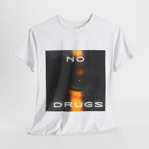 Könnte beinhalten: Weißes T-Shirt mit einem Grafikdruck eines Auges und dem Text "NO DRUGS" in Weiß.