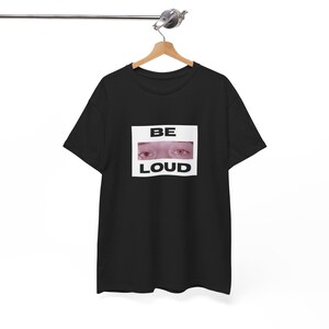 Könnte beinhalten: Schwarzes T-Shirt mit einem weißen Rechteck, auf dem "BE LOUD" steht und ein Bild von einem Augenpaar darin ist.
