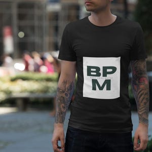 Könnte beinhalten: Ein schwarzes T-Shirt mit einem weißen Quadrat auf der Vorderseite. Das Quadrat enthält den Text "BPM" in grünen Buchstaben mit den Worten "Beats Per Minute" in kleineren weißen Buchstaben darunter.