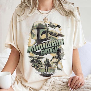K&ouml;nnte beinhalten: Cremefarbenes T-Shirt mit einem Grafikdesign aus der Star Wars-Serie "The Mandalorian and Grogu". Das Design zeigt den Helm des Mandalorianers, Grogu und den Satz "THIS IS THE WAY".