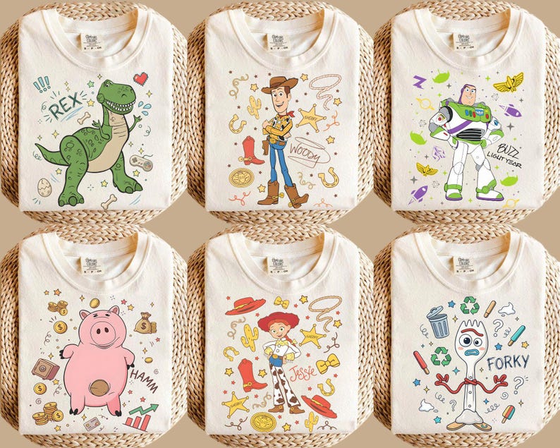 May include: Six off-white t-shirts with colorful cartoon character designs. The designs include a green dinosaur, Woody, Buzz Lightyear, Hamm the pig, Jessie, and Forky. Each shirt is folded and displayed on a woven surface.