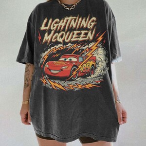 May include: Dark gray t-shirt featuring Lightning McQueen from the Cars movie. The graphic shows the red race car with the number 95, surrounded by lightning bolts and the text "Lightning McQueen".