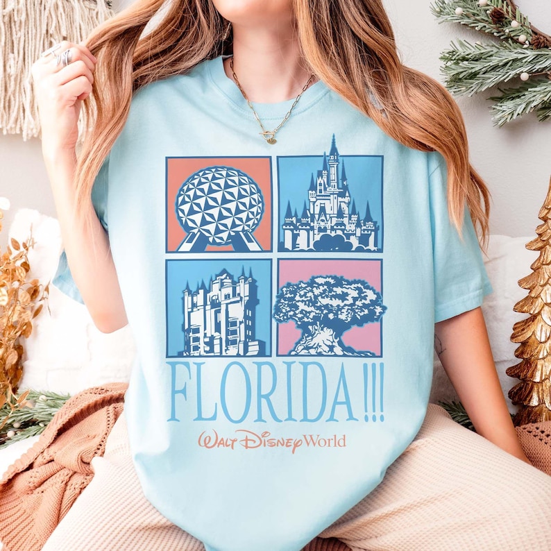 May include: Light blue t-shirt featuring four square graphics with iconic Florida landmarks. The shirt includes the text "FLORIDA!!!" and "Walt Disney World" in a playful font. The shirt is a comfortable, casual style.