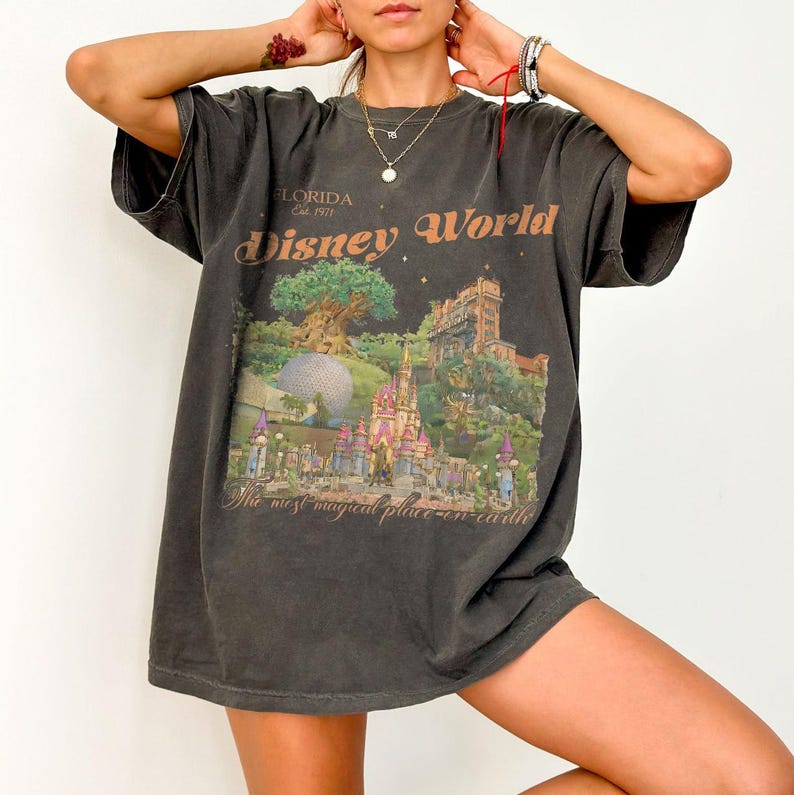 May include: Dark gray t-shirt featuring a colorful Disney World graphic. The graphic includes a castle, Spaceship Earth, and the text "Disney World" and "The most magical place on earth". The shirt is oversized with short sleeves.