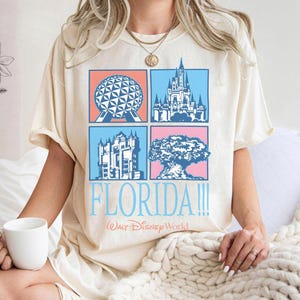 May include: Cream-colored t-shirt featuring four square illustrations of Florida landmarks. The shirt has the word "FLORIDA!!!" in light blue, with "Walt Disney World" below. The shirt is a relaxed fit.