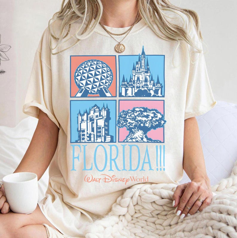 May include: Cream-colored t-shirt featuring four square illustrations of Florida landmarks. The shirt has the word "FLORIDA!!!" in light blue, with "Walt Disney World" below. The shirt is a relaxed fit.