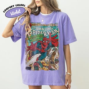Puede incluir: Una camiseta violeta de manga corta con un estampado gr&aacute;fico vintage de Marvel Comics The Amazing Spider-Man en la parte delantera. La portada del c&oacute;mic muestra a Spider-Man con un traje rojo y azul con texto que incluye Marvel Comics Group.
