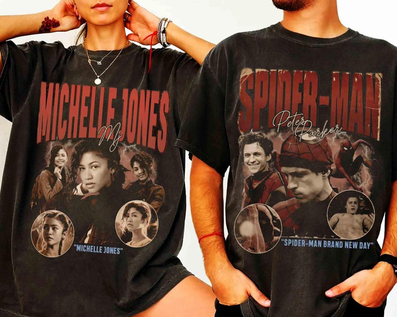 May include: Two dark gray t-shirts featuring movie-themed graphics. One shirt displays "MICHELLE JONES" in red lettering with images of a woman. The other shirt says "SPIDER-MAN Peter Parker" with images of a man.