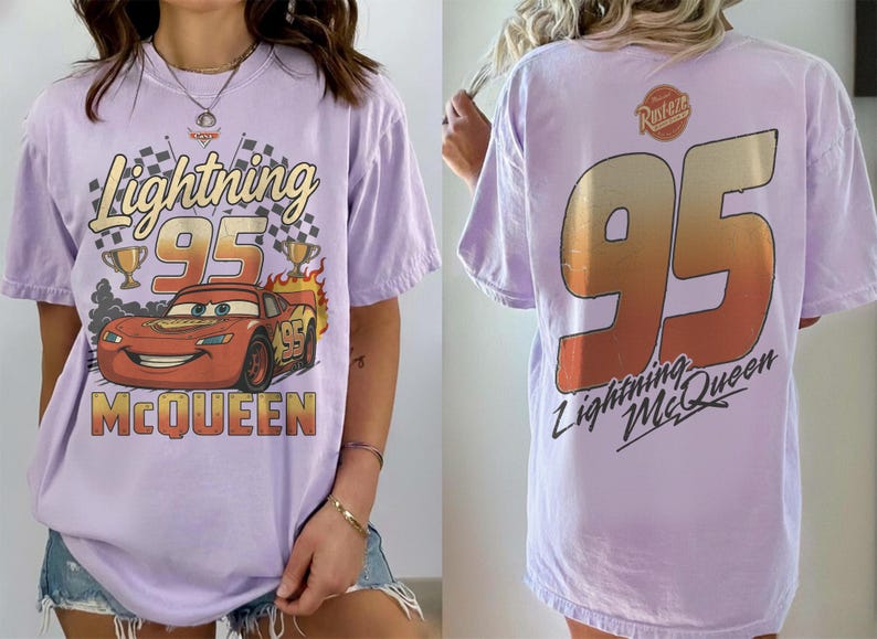May include: A light purple short-sleeve t-shirt featuring a graphic of Lightning McQueen with the text Lightning 95 McQueen on the front. The back displays a large number 95 in a gradient orange and yellow fill with the text Lightning McQueen.