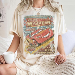 Pu&ograve; includere: T-shirt color crema con grafica vintage di Saetta McQueen del film Cars. La grafica include testo come "Lightning McQueen", "Radiator Springs" e "Winner Takes All". La maglietta ha maniche corte e una vestibilit&agrave; ampia.