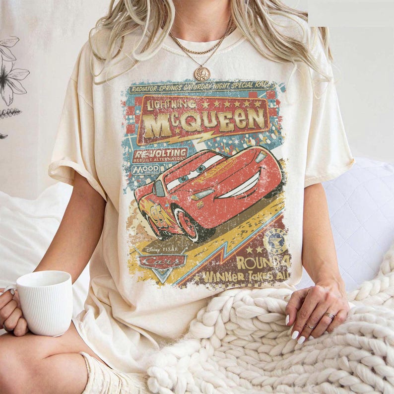 Pu&ograve; includere: T-shirt color crema con grafica vintage di Saetta McQueen del film Cars. La grafica include testo come "Lightning McQueen", "Radiator Springs" e "Winner Takes All". La maglietta ha maniche corte e una vestibilit&agrave; ampia.