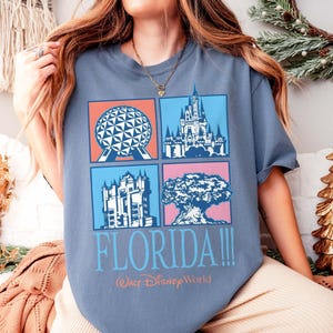 May include: A blue t-shirt featuring four colorful squares with iconic Florida landmarks: Spaceship Earth, Cinderella Castle, Tower of Terror, and the Tree of Life. The word "FLORIDA!!!" and "Walt Disney World" are printed below the squares.