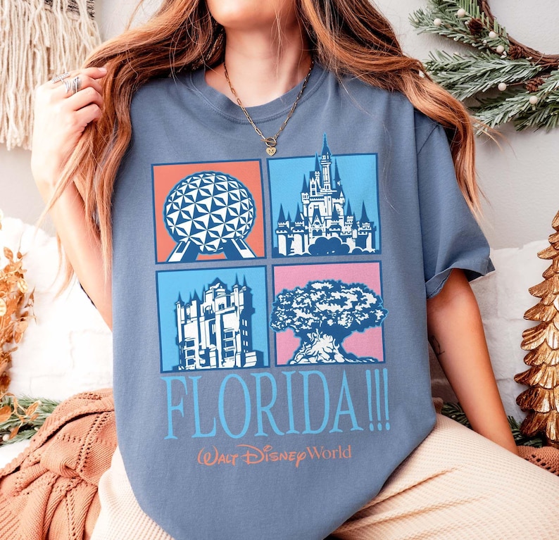 May include: A blue t-shirt featuring four colorful squares with iconic Florida landmarks: Spaceship Earth, Cinderella Castle, Tower of Terror, and the Tree of Life. The word "FLORIDA!!!" and "Walt Disney World" are printed below the squares.