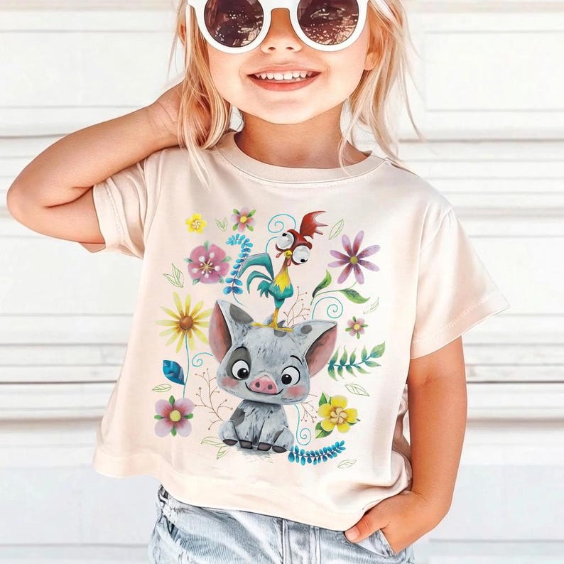 K&ouml;nnte beinhalten: Hellbeige T-Shirt mit einem Cartoon-Schwein und Hahn-Design, umgeben von bunten Blumen und Bl&auml;ttern. Das Design ist auf dem T-Shirt zentriert und wirkt l&auml;ssig. Getragen von einem kleinen Kind.