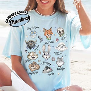May include: Light blue t-shirt with a graphic featuring cartoon characters from a movie. The shirt has the words "COMFORT COLORS" and "Chambray" printed on it. The characters include a fox, a bunny, and a sloth.