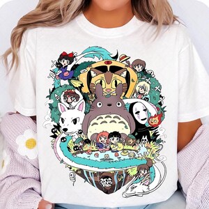 May include: White t-shirt with a colorful graphic print of characters from the Studio Ghibli films. The characters include Totoro, No Face, Kiki's Delivery Service, and others.