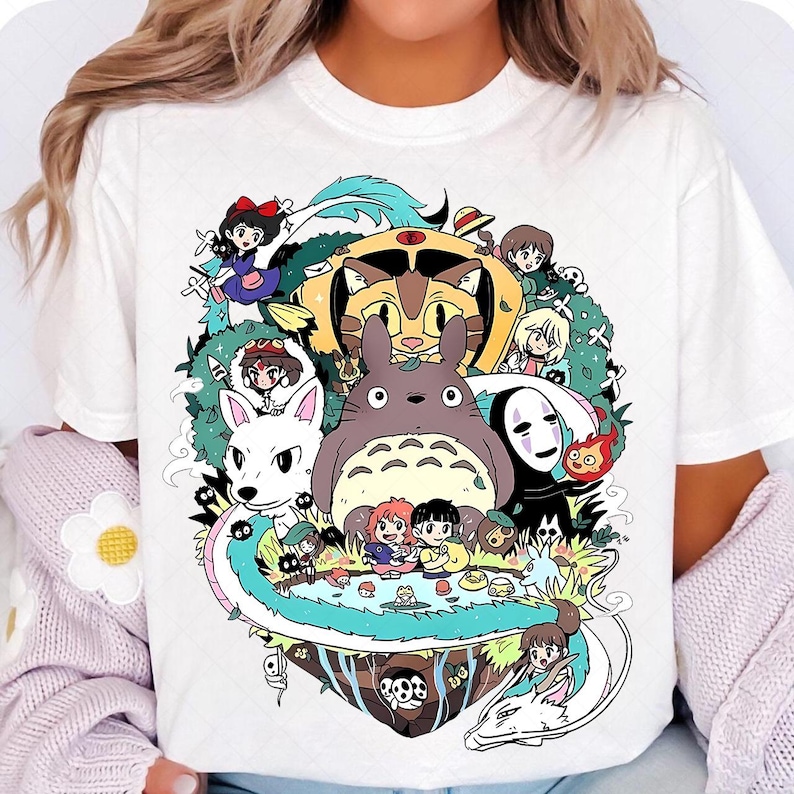 May include: White t-shirt with a colorful graphic print of characters from the Studio Ghibli films. The characters include Totoro, No Face, Kiki's Delivery Service, and others.