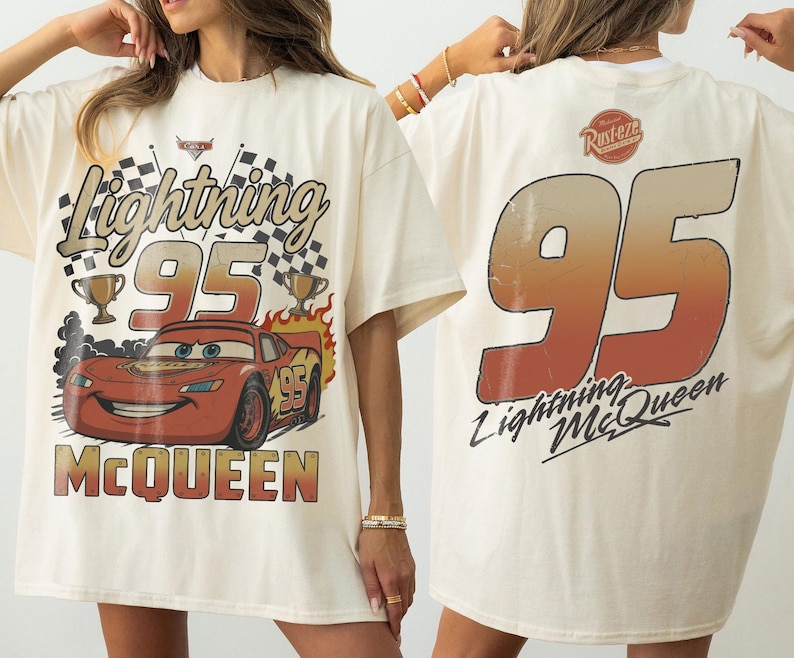 May include: An off-white t-shirt featuring a graphic of Lightning McQueen with the text Lightning 95 McQueen on the front. The back displays a large number 95 in a gradient orange and brown color with the text Rust-eze and Lightning McQueen.