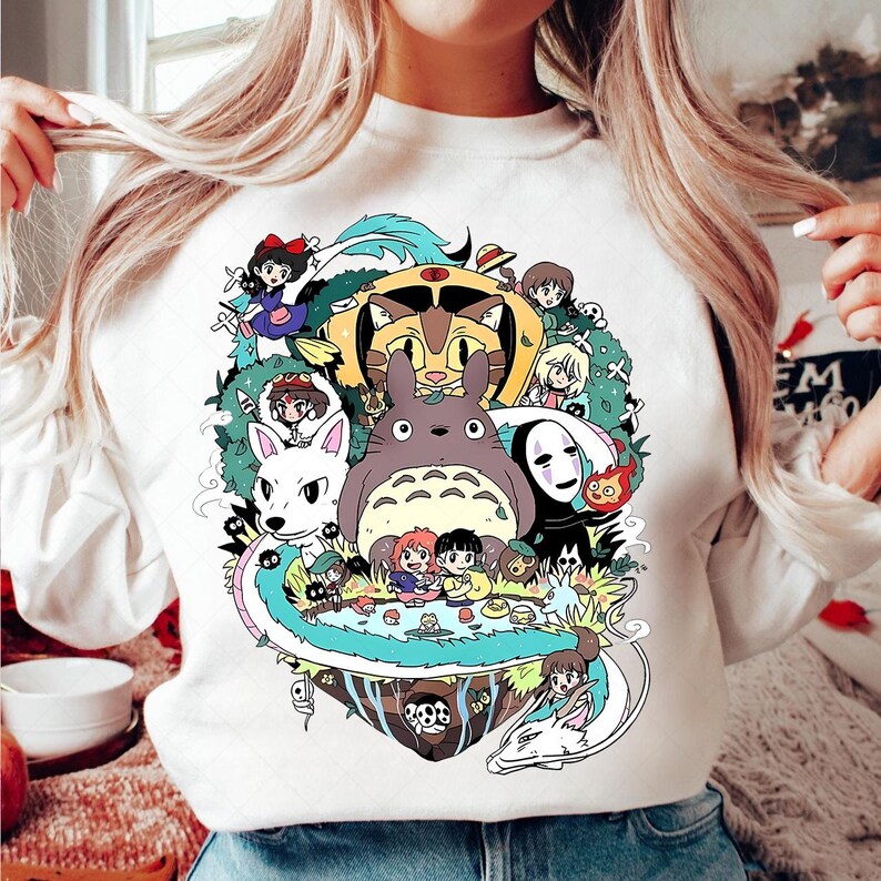 May include: White sweatshirt with a colorful graphic print of characters from the Studio Ghibli film 'My Neighbor Totoro'. The print features Totoro, Catbus, No Face, and other characters from the film.