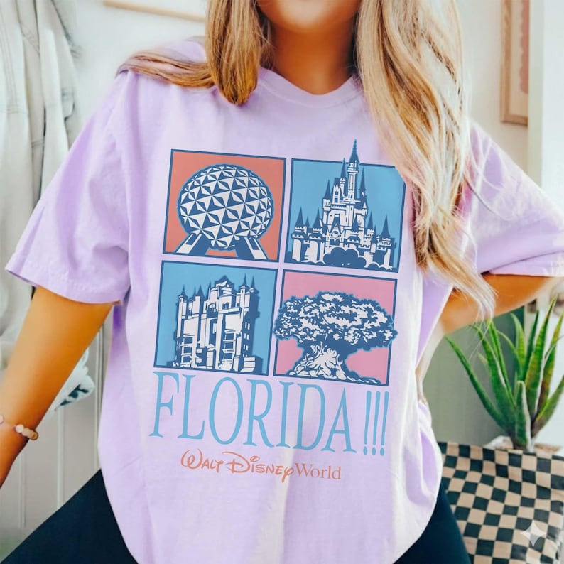 May include: A light purple t-shirt featuring four squares with Disney World icons. The shirt has the word "FLORIDA!!!" in light blue, with "Walt Disney World" below. The shirt is a short-sleeved, casual style.
