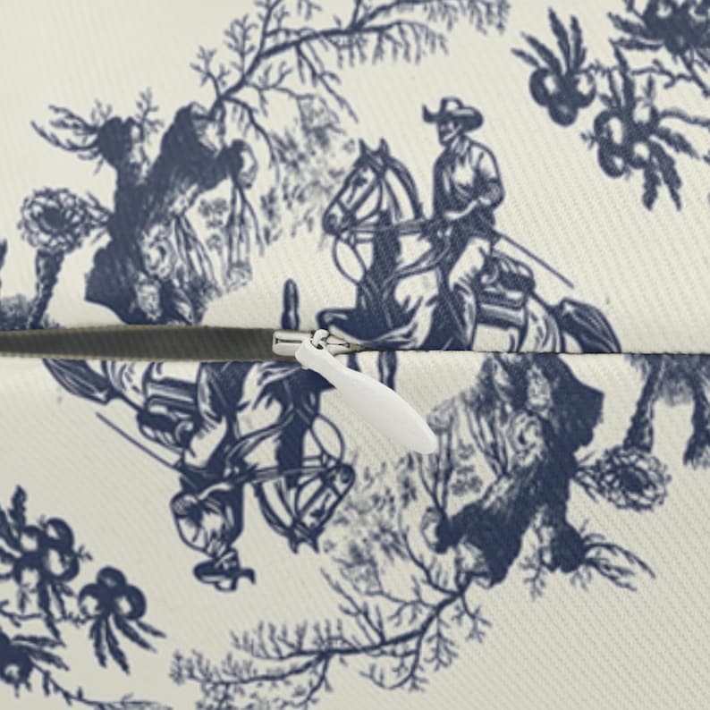 Close-up of the zipper and fabric texture on a cream lumbar pillow with navy blue Western toile print and cowboy detail