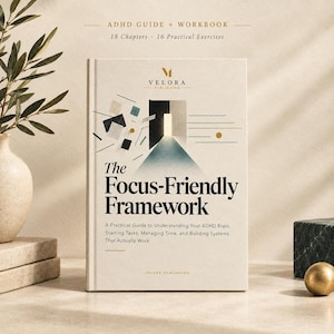 Op de afbeelding: Een hardcover boek getiteld The Focus-Friendly Framework met een crèmekleurige kaft. De voorzijde bevat de tekst ADHD GUIDE + WORKBOOK, 18 Chapters, 16 Practical Exercises en het Velora Publishing logo met een grafische afbeelding van een deur.
