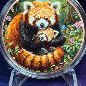 May include: A circular collectible coin featuring a detailed, colorful illustration of an adult red panda holding a small red panda cub. The scene is set against a lush green forest background with small pink and blue flowers surrounding the animals.