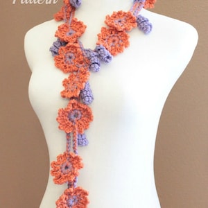 Pode incluir: Um colar de flores de crochê com flores laranja e roxas alternadas. O colar é exibido em um manequim branco.