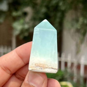 May include: A light blue and white crystal point with a pointed top and a flat base. The crystal has a layered appearance with white and brown inclusions.
