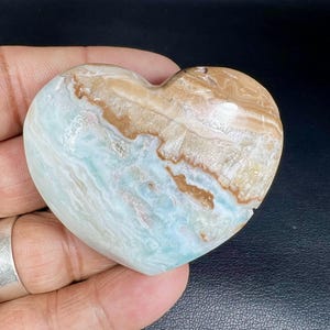 Può includere: Una pietra levigata a forma di cuore con motivi a spirale blu, bianchi e marroni.