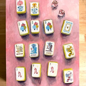 May include: A painting of Mahjong tiles and dice on a pink background. The tiles feature various symbols, numbers, and the word "Joker." The dice are translucent with visible dots. The artwork is a close-up view of the game pieces.
