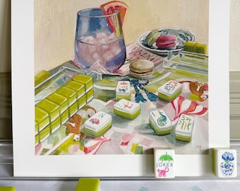 May include: A still life painting depicting a glass of pink liquid with a grapefruit slice, macarons, and green and white Mahjong tiles. The painting is set against a white backdrop, with additional Mahjong tiles in the foreground.
