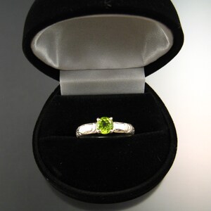 May include: A silver ring with a green gemstone in a black ring box.