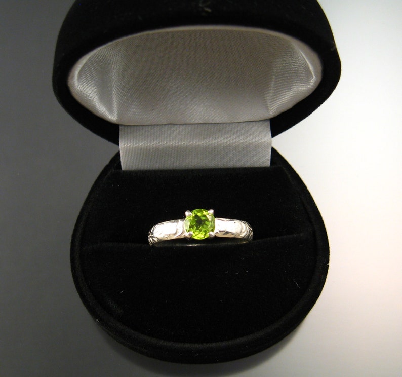May include: A silver ring with a green gemstone in a black ring box.