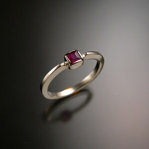 May include: A simple silver band ring with a square-shaped ruby gemstone set in the center.