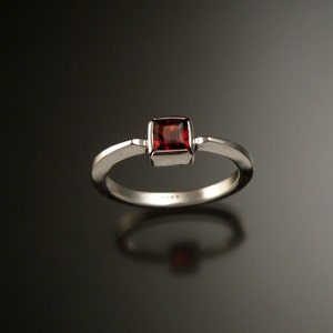 Puede incluir: Un anillo de plata con una piedra preciosa roja de forma cuadrada engastada en el centro.