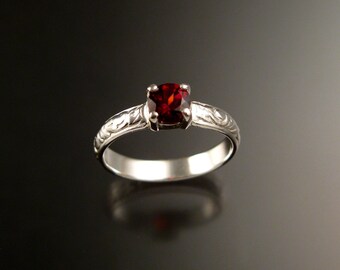 May include: A silver ring with an ornate design and a red gemstone in the center.