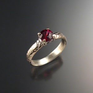 Puede incluir: Un anillo de plata con una piedra preciosa roja oscura engastada en un diseño floral.