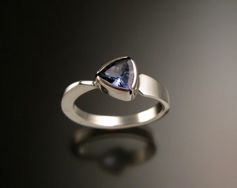 Puede incluir: Un anillo de plata con una piedra preciosa azul triangular engastada en un engaste de bisel. El anillo tiene una banda curva.