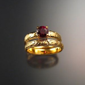 Puede incluir: Un juego de alianzas de boda de oro con una piedra preciosa roja. La banda está grabada con un diseño floral.