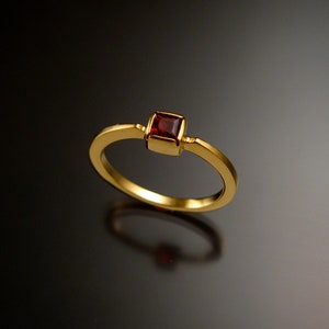 Puede incluir: Un anillo de oro con una piedra preciosa roja cuadrada en el centro.