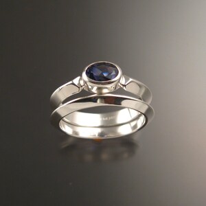 May include: A silver ring set with a dark blue oval gemstone. The ring is a simple band with a slightly raised setting for the stone.