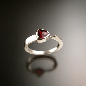 May include: A silver ring with a triangular red gemstone set in a prong setting.