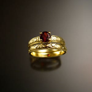 Puede incluir: Un juego de alianzas de boda de oro con una piedra preciosa roja. La banda está grabada con un diseño floral.