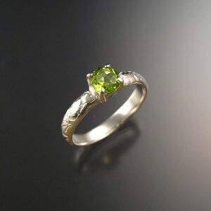 May include: A silver ring with a green gemstone set in a floral design.
